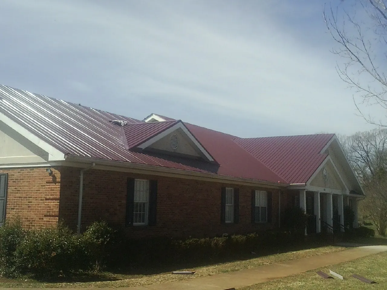 Red metal roof with gabled entries on a long brick building, from a Hail Damage Roof Repair job in Curtice