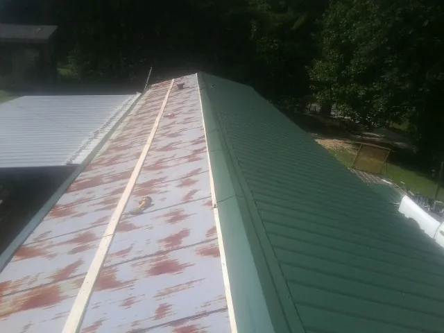 Old rusted panels beside newly installed green metal roofing — Wind Damage Roof Repair by Roofing Brothers in Curtice