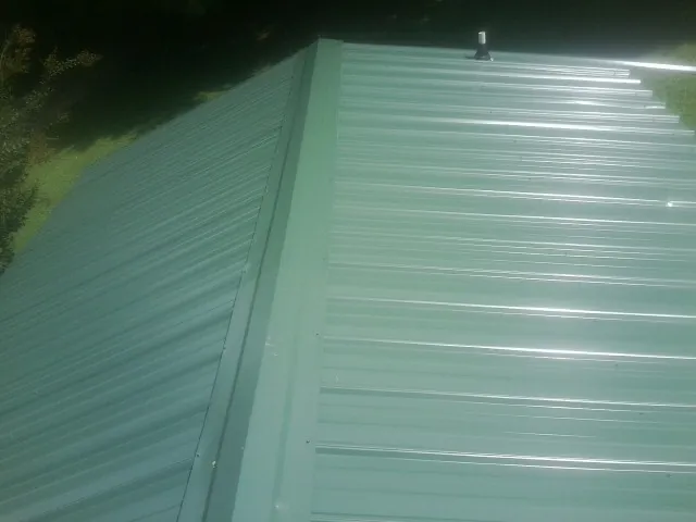 New green metal panels meeting at the ridge of a roof — Flat Roof Repair work by our crew in Curtice