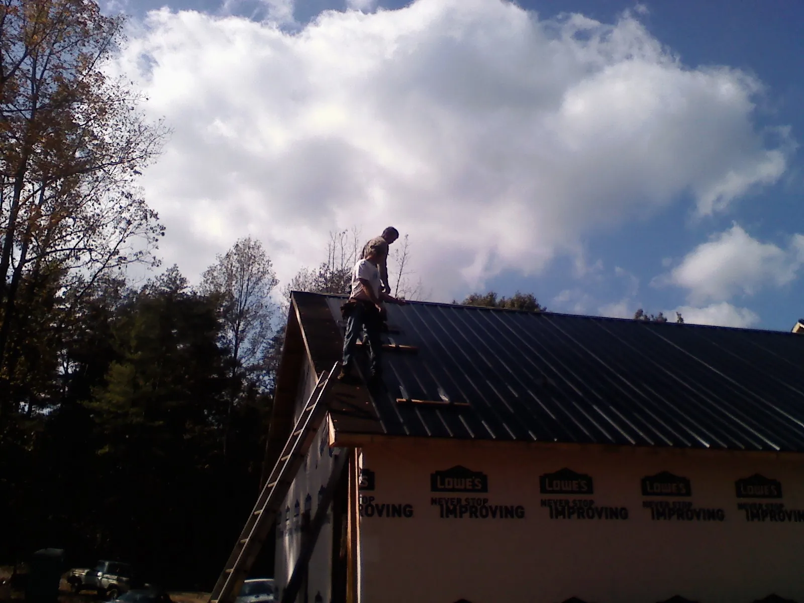 Roofer fastening dark metal panels high against a cloudy sky, from a Roof Inspection job in Curtice