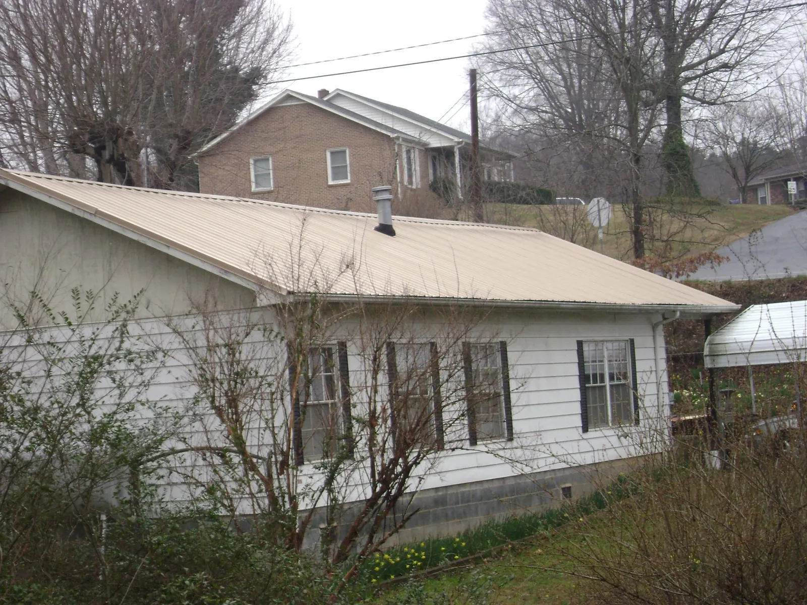 Tan metal roof on a white sided house set into a hillside — Commercial Roofing by Roofing Brothers in Curtice